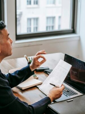 Man using laptop and smartphone for a video call in an office setting.
